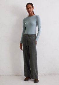 Lange mouwen lichtblauwe top en donkergrijze wijde broek met een elastische tailleband en trekkoord. Glad weefsel en zichtbare zijzakken.
