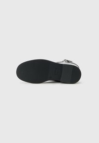 Svart såle på en sølvfarget lær ankle boot med lav hæl og sideklips, vist fra bunnen på en enkel hvit bakgrunn.
