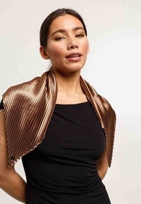 Enveloppe plissée en bronze métallisé avec un bord festonné, portée sur un haut noir, présentant un design élégant et une texture lisse.