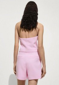 Salopetă roz fără bretele, cu un corset ajustat și pantaloni scurți. Țesătură netedă, cu buzunare la spate și un design structurat.