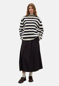 Pull rayé blanc et marine, col roulé côtelé, avec une coupe décontractée. Associé à une jupe noire longueur genoux et des chaussures marron.