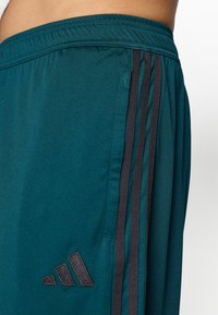Shorts deportivos color aguamarina, hechos de una tela ligera, cuentan con tres franjas negras a lo largo de los lados y un pequeño logo negro en la parte inferior.
