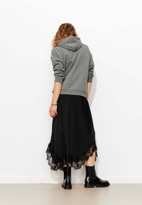 Sweat à capuche gris avec une capuche, associé à une jupe noire ornée d'un bord en dentelle à l'ourlet. Des bottines noires brillantes complètent la tenue.