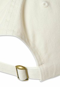 Fehér pamut sapka részlete, látható az állítható pánt és a fém csat. A látható varrás és a texturált anyag tisztaságot és tartósságot biztosít.