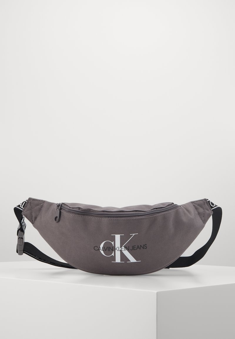 Sac banane en tissu gris Calvin Klein Jeans avec sangle noire réglable et fermeture éclair.