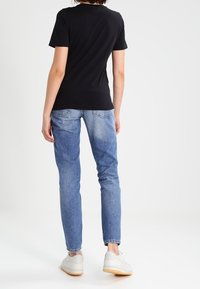 Černé tričko s krátkým rukávem, přiléhavý střih, kombinované se světle modrými džíny. Bílé tenisky s gumovou podešví viděné ze zadu.