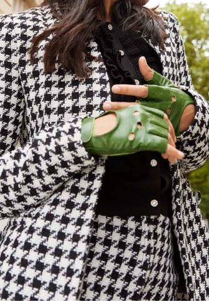 Blazer et pantalon à motif pied-de-poule en noir et blanc, associés à des gants en cuir vert sans doigts, présentant des trous et une texture lisse.