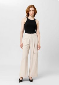 Pantalones de pierna ancha beige con bolsillos laterales, combinados con una camiseta sin mangas negra. La tela parece suave, adecuada para un estilo casual o smart-casual.