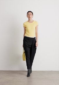 Haut jaune à manches courtes, pantalons noirs ajustés, bottines noires et un sac à main jaune. Design simple avec une texture douce et des couleurs contrastantes.