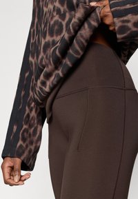 Dlhý rukáv s leopardím vzorom a jemnou textúrou, doplnený o hnedé legíny s vysokým pásom, plochými švami a priliehavým strihom.