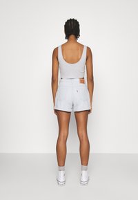 Top gris sin mangas con espalda en forma de scoop, combinado con shorts de mezclilla azul claro con dobladillos enrollados y una etiqueta en la parte trasera. Zapatillas blancas puestas.