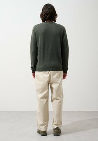 Pull en laine vert olive avec des poignets et un ourlet côtelés, associé à un pantalon ample de couleur crème et des baskets marron, vu de dos.