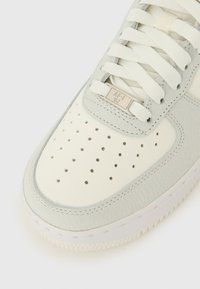 Bijela kožna tenisica s naglascima od svijetlosivog antilopa, perforiranim vrhom, bijelim vezicama i srebrnom metalnom oznakom s natpisom "AF-1 '82."