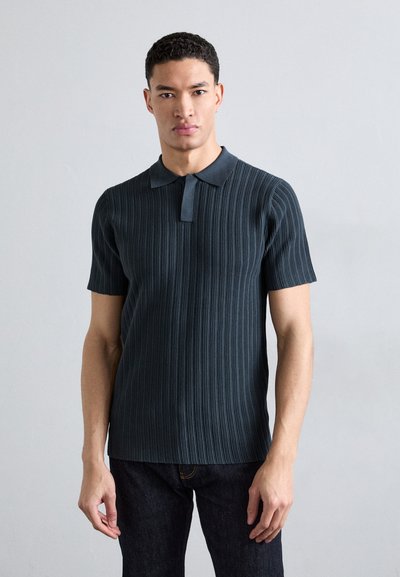 Polo shirt bleu marine à manches courtes avec une texture côtelée verticale et un col contrastant. Porté avec un jean en denim foncé.