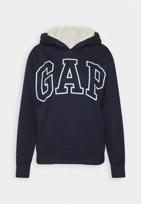 Sweat à capuche bleu marine avec un logo "GAP" blanc et turquoise. Il est doté d'une capuche doublée en polaire douce ainsi que de poignets et d'un ourlet côtelés.