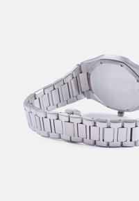 Sølv rustfrit stål ur med et glat, sammenkoblet armbåndsdesign. Bagsiden er flad og har indgraverede detaljer.