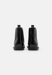 Botines de charol negros con paneles laterales elásticos y tiradores; suelas negras delgadas; acabado liso y brillante.