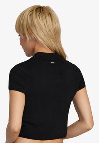 Top corto de manga corta de canalé negro con un cuello clásico y una pequeña etiqueta con el logo en la parte posterior del cuello. Textura suave y diseño ajustado.