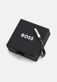 Caja negra con "BOSS" en blanco, que contiene una pulsera de cadena negra con un detalle y cierre en plata.