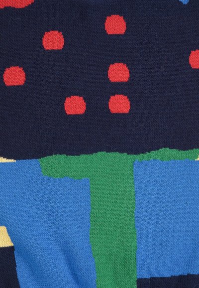 Gros plan d'un tissu avec un motif tricoté présentant des points rouges sur un fond bleu foncé au-dessus de motifs en blocs verts et bleus.