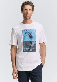 Baltos medvilnės marškinėliai su grafiniu atspaudu, vaizduojančiu sraigtasparnį prieš mėlyną fono, su užrašais "TOM TAILOR" ir "TEAM AERONAUT".
