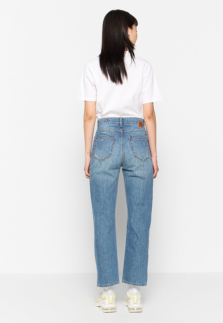 Hochgeschnittene Jeans mit geradem Bein aus hellblauem Denim. Verfügt über fünf Taschen und ein beige Lederpatch auf der Rückseite. Mit einem rohen Saum abgeschlossen.