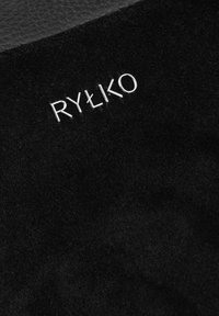Čierny semišový materiál s vyrazeným strieborným logom "RYŁKO". Povrch je hladký s jemnou textúrou a pozadie je tmavé.