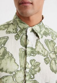 Short-sleeve shirt in light fabric featuring a green floral pattern. Button-down collar and pearl-like buttons enhance its design.