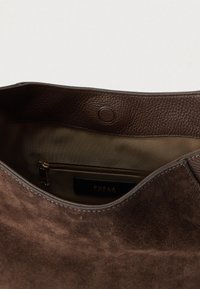 Barna szarvasbőr kézitáska belseje cipzáras zsebbel, sima bőrbéléssel és logós címkével. A textil bélés világosabb bézs színű.