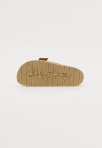 Sandale marron avec une semelle extérieure en caoutchouc texturé présentant un motif géométrique. Comprend une sangle ajustable pour un maintien sécurisé.