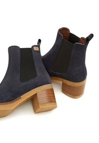 Botines de ante azul marino con paneles laterales elásticos y un tacón de bloque de madera texturizada, con punta redonda y forro interior suave.