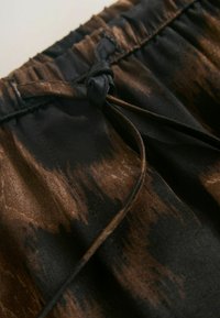 Barna és fekete mintás szövet, megkötő részlettel. Lágy textúrájú, ráncolt derékpánttal, amelyen világos és árnyékos részek váltakoznak.