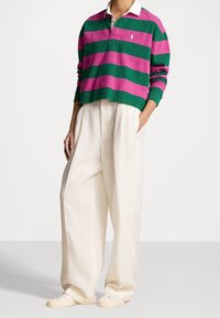 Gestreiftes Polohemd in Pink und Grün mit einem weißen Kragen, kombiniert mit locker sitzenden, cremefarbenen Leinenhosen und lässigen weißen Schuhen.