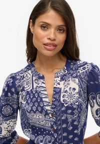 Blaue Bluse mit floralem und paisley-muster, featuring einen V-Ausschnitt, Knopfdetails und puffärmeln.
