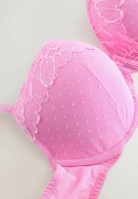 Roosa polsterdatud rinnahoidja pitsilise äärisega. Tassidel on tekstuuriga täpimustrid, rihmad on siledad. Äärte detailne õmblus. Kerge sünteetiline materjal.