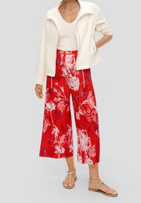 Culottes plissés rouges à motif floral accompagnés d'une veste légère blanche à zip. Le pantalon présente un motif floral audacieux et une coupe décontractée.