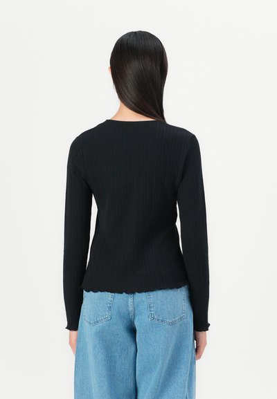 Black long-sleeve ribbed top, featuring a round neckline and scalloped hem. Paired with light blue wide-leg jeans. Textured fabric.