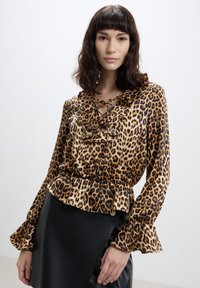 Blusa con stampa leopardata, maniche lunghe, polsini arricciati, scollatura con lacci e vita a peplo. Tessuto setoso con finitura lucida.