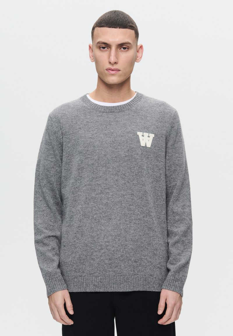 Grauer gestrickter Pullover mit langen Ärmeln, gerippten Bündchen und Saum, mit einem cremefarbenen Buchstaben "W" auf der Brust, rundem Ausschnitt und weicher Textur.
