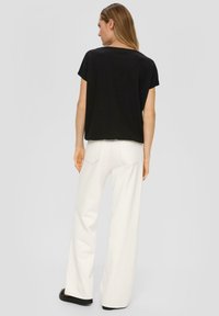 Czarny krótki top z krótkim rękawem w zestawieniu z białymi spodniami o szerokich nogawkach. Posiada luźny krój i teksturowany materiał. Obuwie jest czarne z grubą podeszwą.