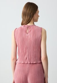 Top senza maniche plissettato color rosa con scollatura rotonda e dettaglio a chiave sul retro, realizzato in un tessuto morbido e texturizzato.