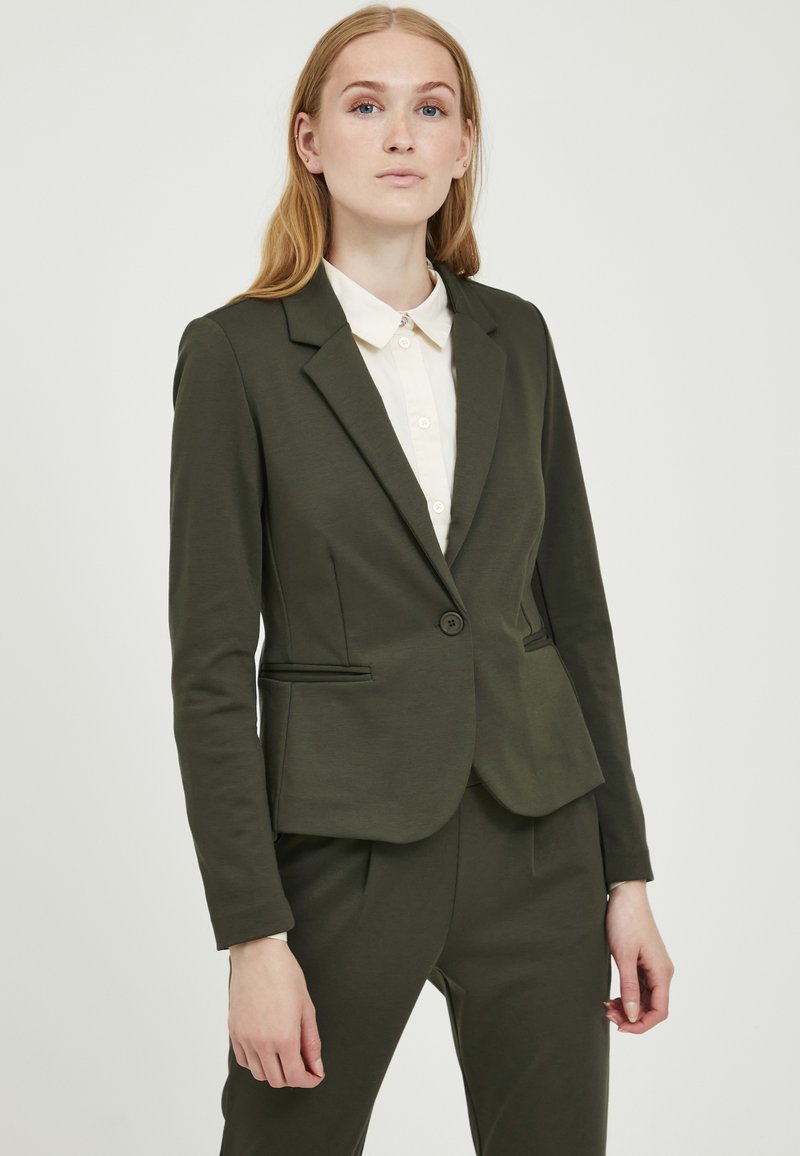 Olive green blazer made from soft fabric, featuring a single button, notched lapels, and two front pockets, paired with a light shirt.
