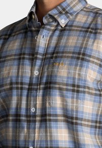 Heren geruite shirt in blauw, bruin en zwart. Beschikt over een button-down kraag, zak en geborduurd detail op de borst. Glad katoen materiaal.