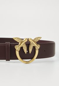 Bordeaux lederen riem met een gouden ronde gesp, versierd met twee gedetailleerde vogelsculpturen die ingewikkelde patronen en texturen tonen.