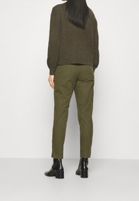 Donkergrijze trui met een gestructureerde afwerking, gecombineerd met olijfgroene broek en zwarte enkelboots met een geribbelde hak, bekeken vanuit de achterkant.