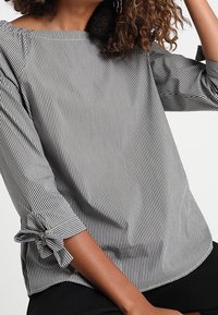 Blusa a righe in bianco e nero, con scollatura quadrata e maniche tre quarti decorate con fiocchi sui polsini.