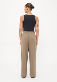 Zwarte mouwloze bodysuit gecombineerd met hoge taille, wijde tan broek, met een gladde textuur en een ontspannen pasvorm.