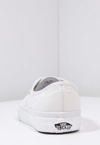 Weiße Leinensneaker mit niedrigem Profil, Gummisohle, genähten Details und "VANS OFF THE WALL"-Logo an der Ferse.