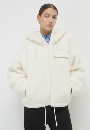 White fleece jacket with a hood, zip closure, and a front pocket. Features drawstrings at the hem and a soft, textured finish.