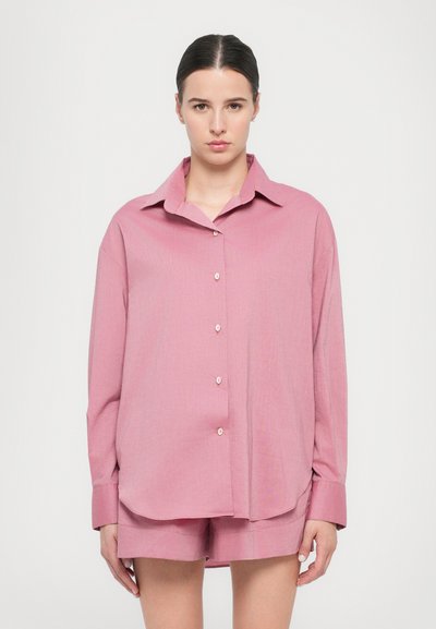 Light pink button-up shirt with long sleeves, pointed collar, and a straight hem, made from a soft fabric with a subtle texture.